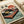 May include: Vintage-style poster print featuring a retro turntable in red and mint green colors with Japanese text, cherry blossom branches, and a stylized sun. The artwork has a weathered, aged appearance and is shown unframed on white paper next to a rolled paper tube on a light wooden surface.