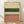 May include: Framed abstract art print with horizontal color bands in cream, forest green, white, and terracotta pink, featuring black polka dot patterns in the middle sections. Wooden frame sits on light hardwood flooring against white walls with natural window light casting soft shadows.