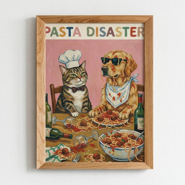 Framed vintage-style illustration showing a tabby cat wearing a white chef's hat and bow tie alongside a golden retriever in sunglasses and bandana sitting at a wooden table covered with spilled spaghetti and meatballs. Wine bottles, overturned glasses, and pasta dishes create a messy dinner scene against a pink background. The text "PASTA DISASTER" appears at the top in colorful letters. Natural wood frame on white wall.