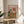 May include: Framed poster propped on round wooden side table next to beige upholstered chair. Artwork shows tabby cat wearing white chef's hat and golden retriever in sunglasses and bandana sitting at table covered with spilled spaghetti, wine bottles, and messy pasta dishes. Colorful title reads "PASTA DISASTER" above pink background. Natural lighting creates soft shadows in neutral-toned room setting.