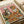 May include: Vintage-style poster print on white paper showing a tabby cat wearing a chef's hat and bow tie sitting at a wooden table with a golden retriever wearing sunglasses and bandana. Both pets are surrounded by messy spaghetti and meatballs, wine bottles, and pasta dishes scattered across the table. The illustration has a pink background with colorful "PASTA DISASTER" text at the top in a retro design style.