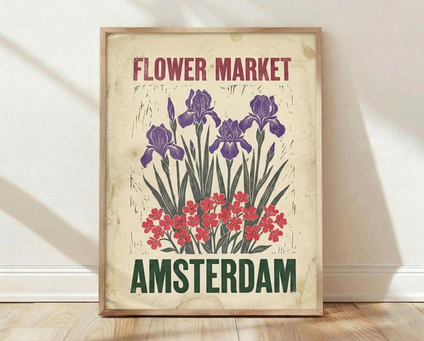 May include: Vintage-style poster with cream aged background featuring purple iris flowers and red blooms, text reading "Flower Market" in burgundy and "Amsterdam" in green, displayed in light wood frame leaning against white wall on wooden floor with natural lighting and soft shadows
