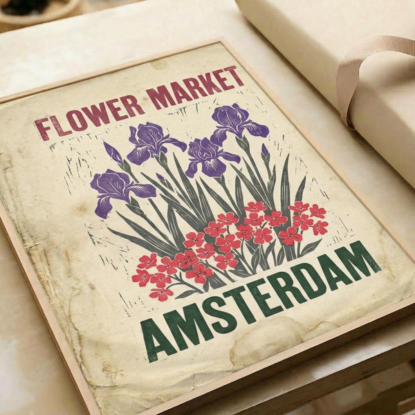 Vintage-style poster print featuring purple irises and red flowers with green foliage on aged cream background. Text reads "FLOWER MARKET" in burgundy letters at top and "AMSTERDAM" in green letters at bottom. Print shown flat on white paper with ribbon visible, displaying weathered texture and distressed edges in linocut or woodblock art style.