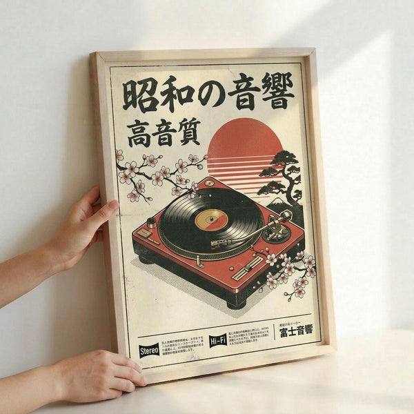 May include: Hands holding a framed vintage-style Japanese poster featuring a red turntable with cherry blossom branches, a red sun, and bonsai tree against cream background. Black Japanese text at top, wooden frame, displayed against white wall.