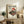 May include: Vintage-style Japanese poster featuring red turntable with vinyl record, cherry blossoms, and setting sun, displayed in light wood frame on rustic wooden sideboard. Room shows cream walls, fern plant, ceramic vase, stacked books, and brown leather chair arm visible in foreground.