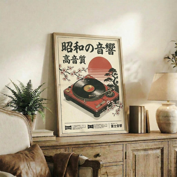 May include: Vintage-style Japanese poster featuring red turntable with vinyl record, cherry blossoms, and setting sun, displayed in light wood frame on rustic wooden sideboard. Room shows cream walls, fern plant, ceramic vase, stacked books, and brown leather chair arm visible in foreground.