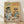 May include: Framed vintage-style poster with yellow background showing two anthropomorphic cats at cafe table. Left cat wears black beret and striped shirt, reading "Cat Tales" newspaper while holding coffee cup. Right orange tabby cat wears sunglasses and tropical floral shirt, holding coffee and croissant. Table displays moka pot, pastries, and checkered tablecloth. Natural wood frame, displayed against white wall on light wooden floor with soft natural lighting.