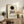 May include: Framed Kandinsky exhibition poster with black circle and geometric shapes in blue, yellow, and red tones, displayed on rustic wooden sideboard beside fern plant, ceramic vase, and stacked books in neutral-toned living room with leather armchair