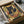 May include: Framed poster print featuring a black cat with golden eyes eating ramen noodles from a red bowl, depicted in vintage Japanese advertising style with warm earth tones and Japanese text. Print shown in black frame inside cardboard shipping box with protective tissue paper wrapping.