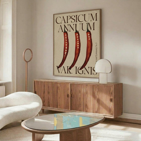 May include: Modern living room interior featuring botanical wall art displaying three red chili peppers with white seeds against cream background, hung above mid-century walnut credenza. Scene includes white curved chair, brass floor lamp, round glass coffee table with colorful abstract art, and natural lighting creating shadows on neutral walls.