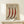 May include: Vintage-style botanical poster in light wood frame showing three red chili peppers with white dots and text "CAPSICUM ANNUUM" and "VAR IGNIS" on cream background. Frame sits on white wooden surface next to small wrapped gift with green sprig against white wall.