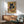 May include: Framed poster print displayed above wooden credenza featuring black cat with yellow eyes eating from ramen bowl with chopsticks, Japanese-inspired design with geometric patterns in warm earth tones including green, gold, and rust colors, shown in modern living room with mint green mid-century chair and small table lamp