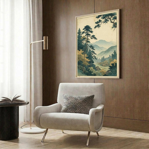 May include: Framed Japanese landscape print featuring mountain valley with pine trees in blue-green tones, displayed on wood paneled wall above modern beige armchair with geometric pillow, brass floor lamp and dark side table with open book nearby
