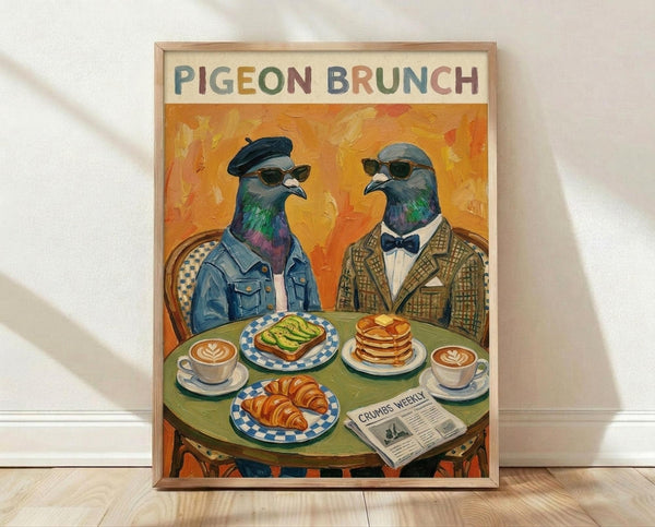 May include: Framed poster print leaning against white wall on light wood floor. Artwork shows two anthropomorphic pigeons wearing sunglasses and vintage clothing sitting at green round table with brunch items including avocado toast, croissant, pancakes, and coffee cups. Orange painted background with "PIGEON BRUNCH" text at top in colorful letters. Natural wood frame, warm lighting with soft shadows.