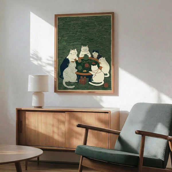 May include: Framed poster showing cats gathered around a small table with yarn balls in Japanese woodblock print style. Green textured background with cats in white, black, and gray colors. Wooden frame hung above mid-century modern walnut credenza with white ceramic lamp. Green upholstered chair with wooden arms sits nearby in sunlit room with white walls.