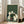 May include: Framed art print in light wood frame showing six cats gathered around a green table with yarn balls and knitting supplies, styled as a parody of classic poker paintings. Green textured background with horizontal line pattern. Print displays in bright living room setting next to beige sectional sofa and large windows with natural lighting on hardwood floors.