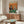 May include: Framed poster showing two cats dressed as humans playing poker at a green felt table with chips and cards, displayed above a mid-century modern walnut credenza in a contemporary living room with white walls, cream chair, and glass coffee table