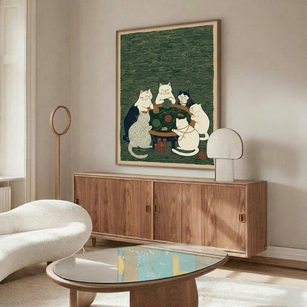 May include: Framed poster print hanging above wooden credenza showing cartoon cats gathered around table with green yarn balls in Japanese woodblock print style with green textured background. Modern living room setting with white curved chair, glass coffee table, floor lamp, and neutral walls.