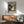 May include: Vintage-style poster featuring turntable illustration with Japanese text hangs in wood frame above mid-century modern credenza. Mint green upholstered armchair with wooden arms sits beside small round table with white ceramic lamp. Warm sunlight creates geometric shadows on white wall in minimalist living room setting.
