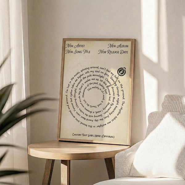 May include: Wood-framed poster with cream background displaying song lyrics arranged in a circular pattern around a small record icon. Text reads "New Artist," "New Album," "New Song Title," and "New Release Date" at top, with "Custom Text Goes Here (Optional)" at bottom. Frame sits on round wooden side table next to beige upholstered chair with decorative pillow, green plant visible in corner, soft natural lighting creating shadows on white wall.