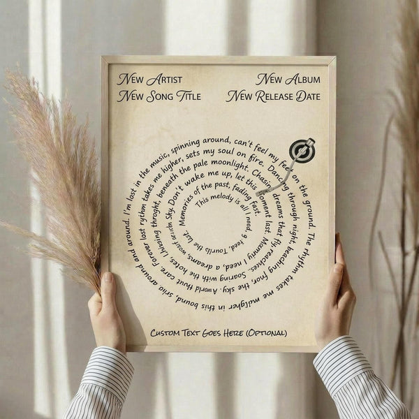 May include: Hands holding a framed beige poster with curved text arranged in a spiral pattern around a vinyl record icon. The frame is light wood, and dried pampas grass is visible on the left side. The poster has placeholder text for customizable song lyrics in black script font against a cream textured background.