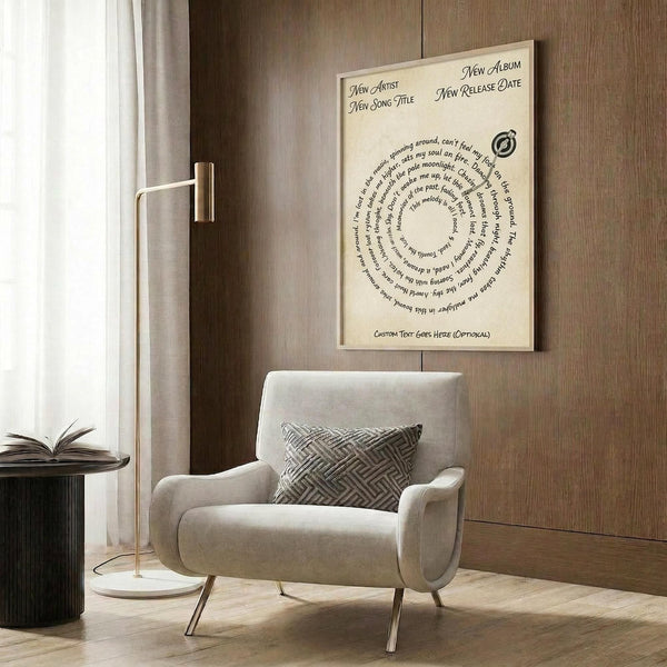 May include: Cream-colored poster with spiral text design and circular logo mounted on wood-paneled wall above beige upholstered armchair with geometric patterned pillow. Modern living room setting features gold floor lamp, dark round side table with open book, and natural lighting from window with white curtains.