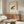 May include: Traditional Japanese ink wash painting of a spotted brown and black frog on aged cream paper with red seal stamps, displayed in thin wooden frame above walnut mid-century credenza. Modern white sculptural chair and glass-top oval coffee table with wood base complete the minimalist room scene with neutral walls and natural lighting.