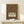 May include: Framed Arts and Crafts style poster featuring ornate floral border with birds, flowers, and foliage in rich burgundy, green, and gold tones. White text panel reads "Art & Socialism" with exhibition details. Natural wood frame displayed on light wooden console with small wrapped gift. Cream colored wall background.