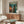 May include: Framed anime poster featuring a character in brown jacket standing by window overlooking neon-lit cityscape, displayed above mid-century walnut credenza in modern living room with white curved chair, glass coffee table, and minimalist decor