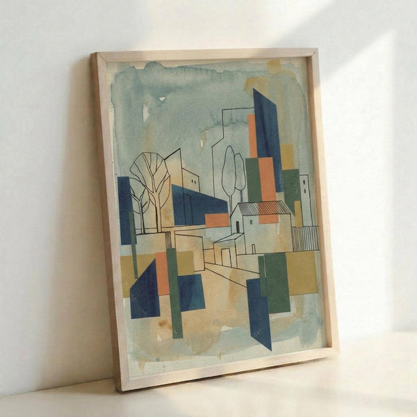 A framed abstract modernist artwork featuring geometric buildings and architectural forms in muted blues, oranges, greens, and beige tones. The composition includes simplified trees, angular structures, and overlapping geometric shapes creating a cubist-style cityscape. The piece has a soft watercolor-like background with defined linear elements throughout. The artwork is displayed in a natural wood frame, leaning against a white wall.