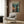 May include: Framed anime poster showing character in futuristic cityscape with Japanese text, displayed on wood paneled wall above beige armchair with geometric pillow, gold floor lamp and side table with open book nearby, modern minimalist room setting