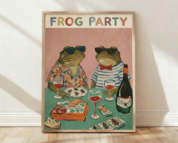 May include: Framed poster print leaning against white wall on light wood floor. Artwork shows two anthropomorphic frogs wearing sunglasses and clothing at a dinner table - one in floral Hawaiian shirt, one in striped shirt with red bow tie. They're sharing wine and food including what appears to be insects on plates. Pink background, teal table surface. Title reads "FROG PARTY" in colorful letters. Natural wood frame.