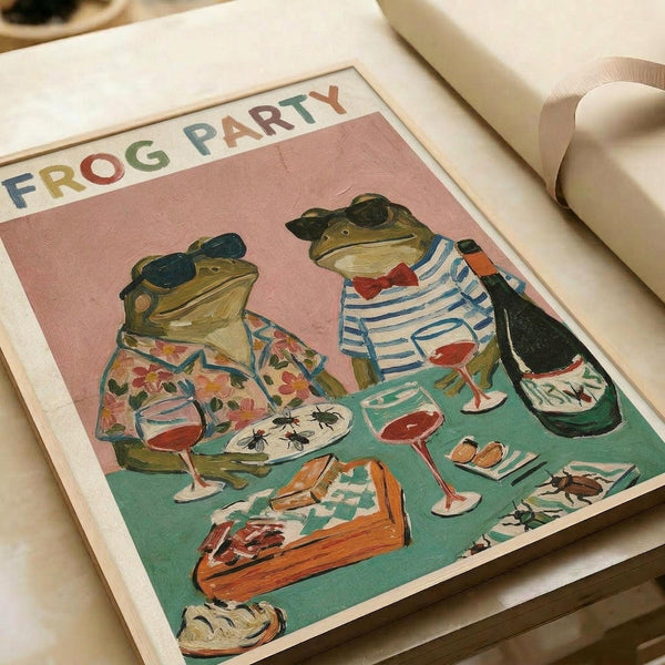 Two anthropomorphic frogs wearing sunglasses sit at a turquoise table having dinner. The left frog wears a floral shirt, the right wears blue and white stripes with a red bow tie. They hold wine glasses while dining on insects from white plates. A slice of cake sits on the table. The illustration has a pink background with "FROG PARTY" text at the top in colorful letters. The artwork appears as a framed print with white matting.