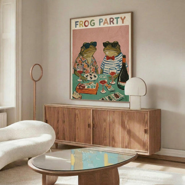 May include: Whimsical illustrated poster showing two frogs wearing sunglasses and casual clothing seated at a green checkered table with wine glasses, food, and a bottle. The artwork features a coral pink background with "FROG PARTY" text at top in colorful letters. Displayed in thin wooden frame above mid-century modern walnut credenza in minimalist living room with white curved chair, brass floor lamp, and glass-top oval coffee table.