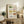 May include: Watercolor illustration of vintage casserole dishes and baking containers in various colors including green, pink, yellow, orange, and blue with floral patterns, displayed in a light wood frame on a rustic wooden sideboard alongside potted ferns, books, and ceramic vases in a cozy living room setting with warm natural lighting.