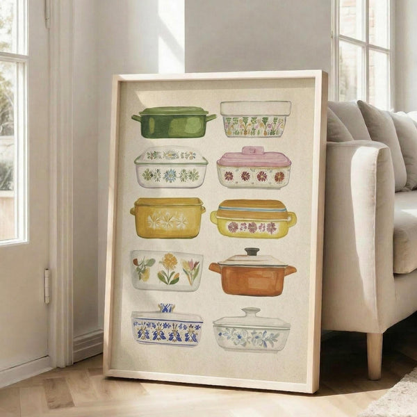 May include: Framed wall art displaying ten vintage-style casserole dishes in watercolor illustration, featuring colorful cookware with floral patterns in green, pink, yellow, orange and blue tones against cream background, shown in light wood frame leaning against white wall next to beige sofa in bright living room with large windows
