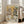 May include: Framed poster print leaning against white wall next to beige armchair in bright room with large windows. Artwork shows two anthropomorphic dogs having tea - a poodle in floral dress with pearl necklace holding teacup, and bulldog in green vest with bow tie. Table set with tiered serving stand, sandwiches, pastries, and floral china tea service. Colorful "DOGS' TEA PARTY" text at top. Vintage illustration style with warm tones.