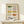 May include: Framed watercolor illustration of ten vintage casserole dishes arranged in rows, featuring various patterns and colors including green, yellow, pink, and floral designs. The artwork is displayed in a light wood frame on a cream-colored shelf next to a small wrapped gift with evergreen sprig, against a white wall.