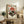 May include: Framed vintage-style poster featuring red turntable with vinyl record against orange sunset with cherry blossoms and Japanese text, displayed on rustic wooden sideboard alongside fern plant, ceramic vase, and books in cozy living room with beige chair and neutral walls
