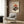 May include: Framed vintage-style poster featuring turntable with vinyl record, orange sunset, Mount Fuji silhouette, and Japanese cherry blossoms, displayed on wood-paneled wall above beige armchair with geometric pillow, gold floor lamp, and side table with open book in modern living room setting