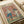 Two anthropomorphic ducks in yoga poses on a vintage-style poster with pink background. One duck in blue pants performs a standing pose with wings raised, while another duck in darker clothing sits in meditation position near a bowl of eggs. A small Buddha statue sits in the corner beside a water bottle. The poster has "DUCK YOGA" text at the top in colorful letters and appears to be displayed in an open book or portfolio with cream-colored pages.
