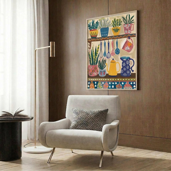 May include: Colorful folk art style poster displaying kitchen shelves with potted plants, hanging utensils, teapot, and decorative vessels in vibrant blues, yellows, pinks and greens. Mounted on wood-paneled wall above beige upholstered chair with geometric pillow. Modern brass floor lamp and dark side table with open book complete the cozy reading corner scene.
