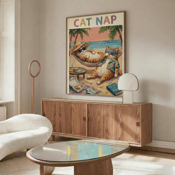 May include: Framed poster displaying cartoon cats relaxing on a tropical beach - one orange tabby lounging in a hammock wearing sunglasses and hat, another cat in Hawaiian shirt sitting nearby. Scene shows palm trees, ocean sunset, beach items scattered around. Poster hangs above mid-century modern wood credenza with white sculptural chair and glass coffee table in minimalist living room with cream walls.