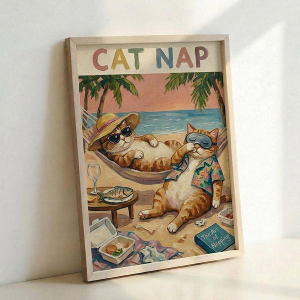 Framed poster artwork showing two cartoon cats relaxing on a tropical beach. One orange tabby cat wearing sunglasses and a straw hat lounges in a hammock, while another orange cat in sunglasses and a Hawaiian shirt sits nearby. The beach scene includes palm trees, blue ocean, sandy shore, a small table with fish and wine glass, scattered books, and a lunch box. The poster has "CAT NAP" text at the top in colorful letters against a cream background. Light wooden frame, leaning against white wall.