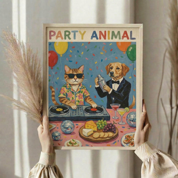 May include: Hands holding a framed poster showing a cat DJ in Hawaiian shirt and sunglasses at turntables next to a dog bartender in tuxedo with cocktail shaker. Colorful party scene with balloons, confetti, cheese platter, cocktails, and disco balls on blue background. Natural wood frame, dried pampas grass visible, neutral curtained interior setting.