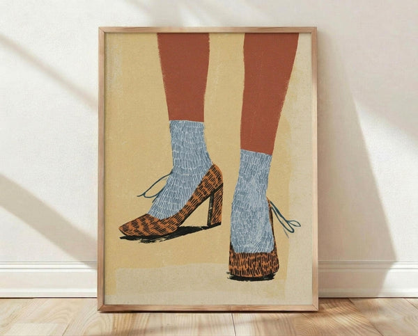 May include: Framed art print showing two legs wearing blue ribbed socks and leopard print Mary Jane shoes with block heels and ankle straps, illustrated in a vintage pop art style with warm yellow background, displayed in light wood frame leaning against white wall on wooden floor