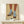 May include: Framed artwork displaying two legs wearing brown pants and blue cable-knit socks with leopard print heeled shoes, rendered in a vintage illustration style with muted colors on cream background. Natural wood frame sits on light wooden surface beside small wrapped gift with evergreen sprig against neutral wall.