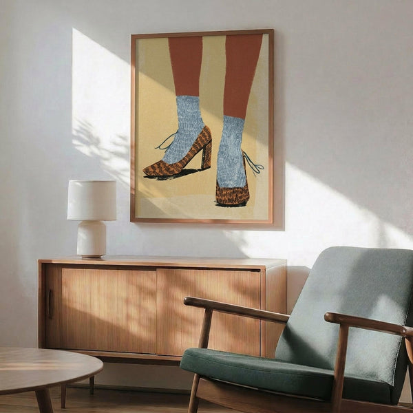 May include: Framed poster showing two legs wearing blue ribbed socks and brown leopard print high heels against a cream and yellow background with rust-colored leg silhouettes. Modern mid-century living room setting with sage green armchair, wooden sideboard, white ceramic lamp, and warm sunlight streaming across white walls.