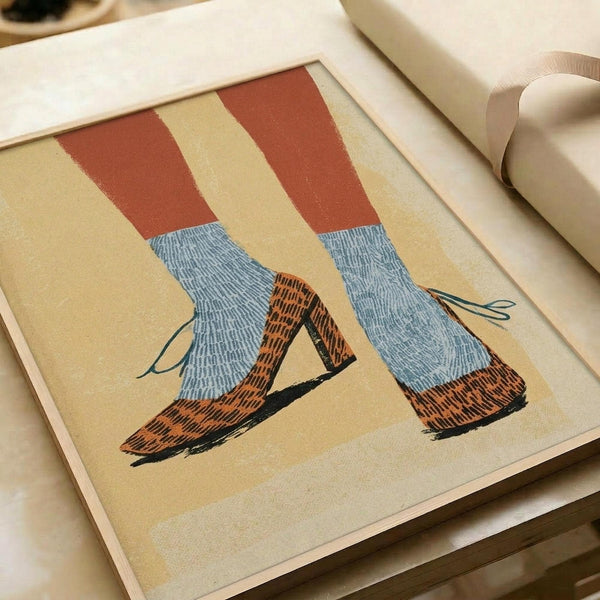 May include: Framed print showing illustration of legs wearing blue textured socks and orange-brown patterned high heel shoes against cream background, displayed on white surface next to white ribbon, warm lighting