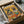 May include: Framed poster print in brown cardboard shipping box with protective wrapping. Colorful illustration shows two French Bulldogs in Mexican attire - one wearing striped poncho with lime, another in floral headband and embroidered top. Orange and yellow background features tacos, guacamole bowl, tequila bottle, margarita glass, and tortilla chips scattered around the festive scene.